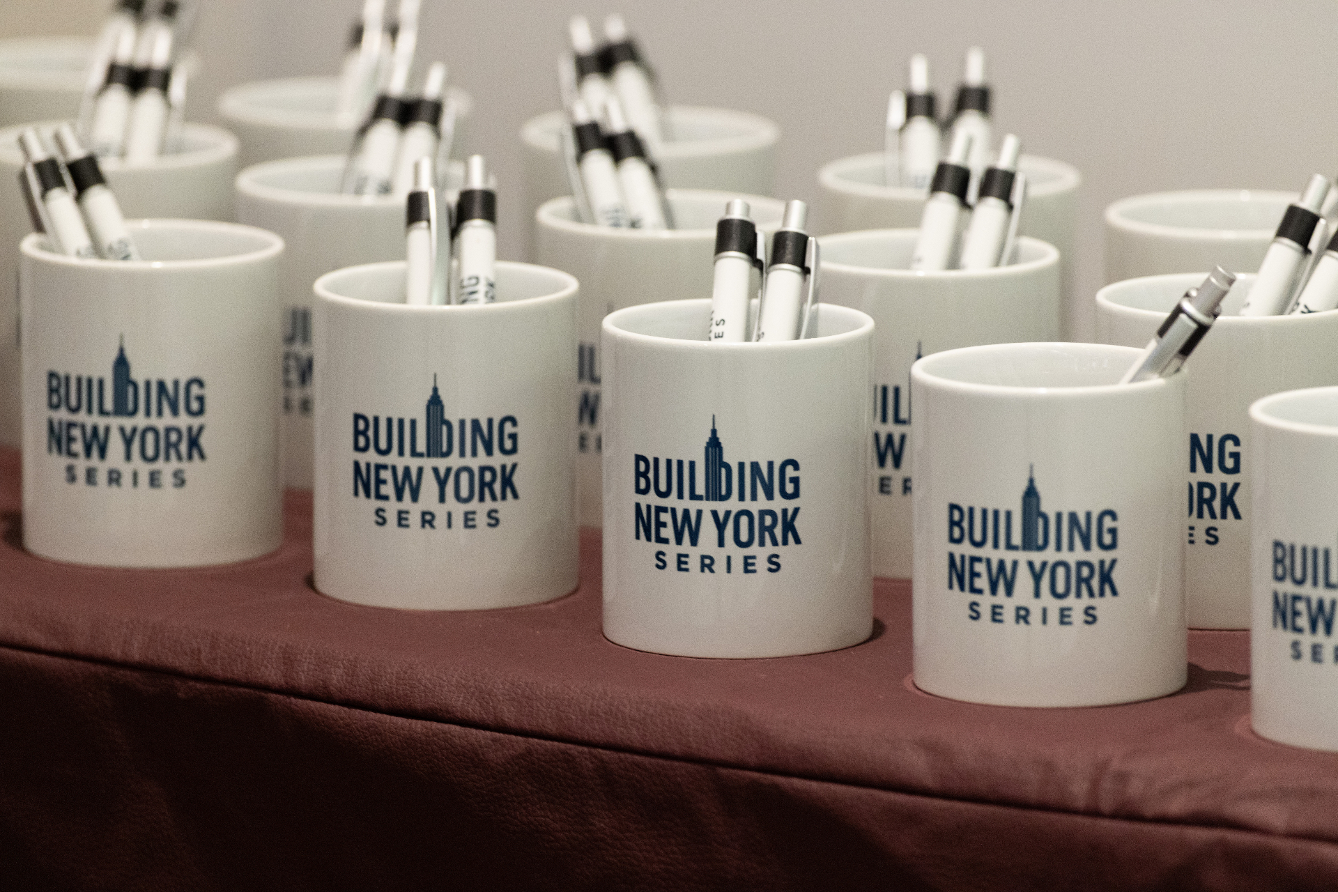 Building New York Series branded mugs with pens arranged for attendees at the airport development event